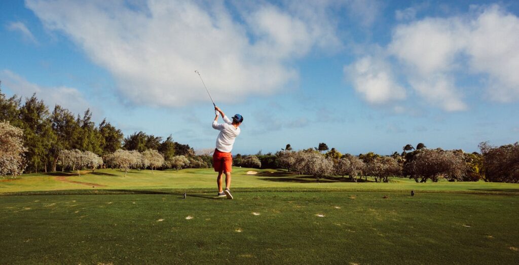 Golfer swinging on a picturesque golf course with lush greenery and clear blue sky