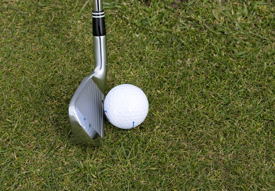 A golf iron positioned beside a ball on the fairway grass, ready for an approach shot